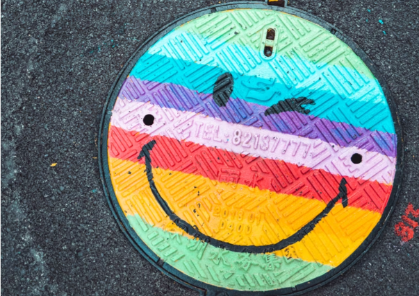 A rainbow smiley face painted on to a manhole cover in the road